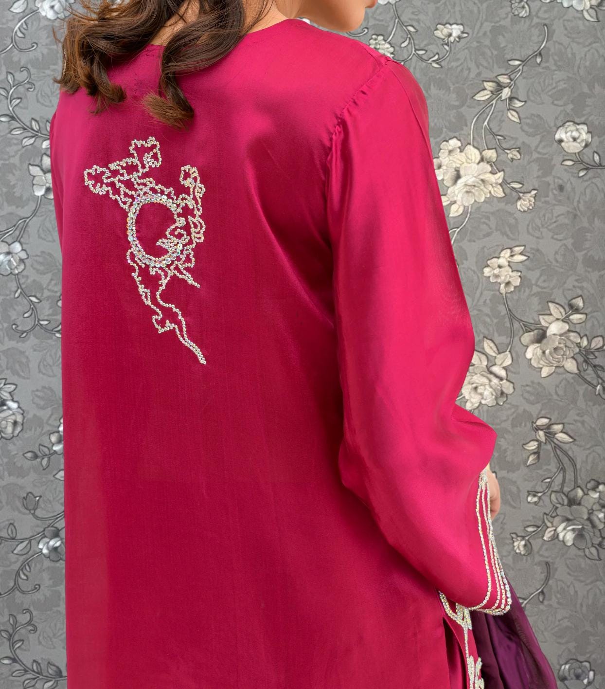 a close-up view of a person wearing a bright pink dress with a white floral embroidered design on the back.