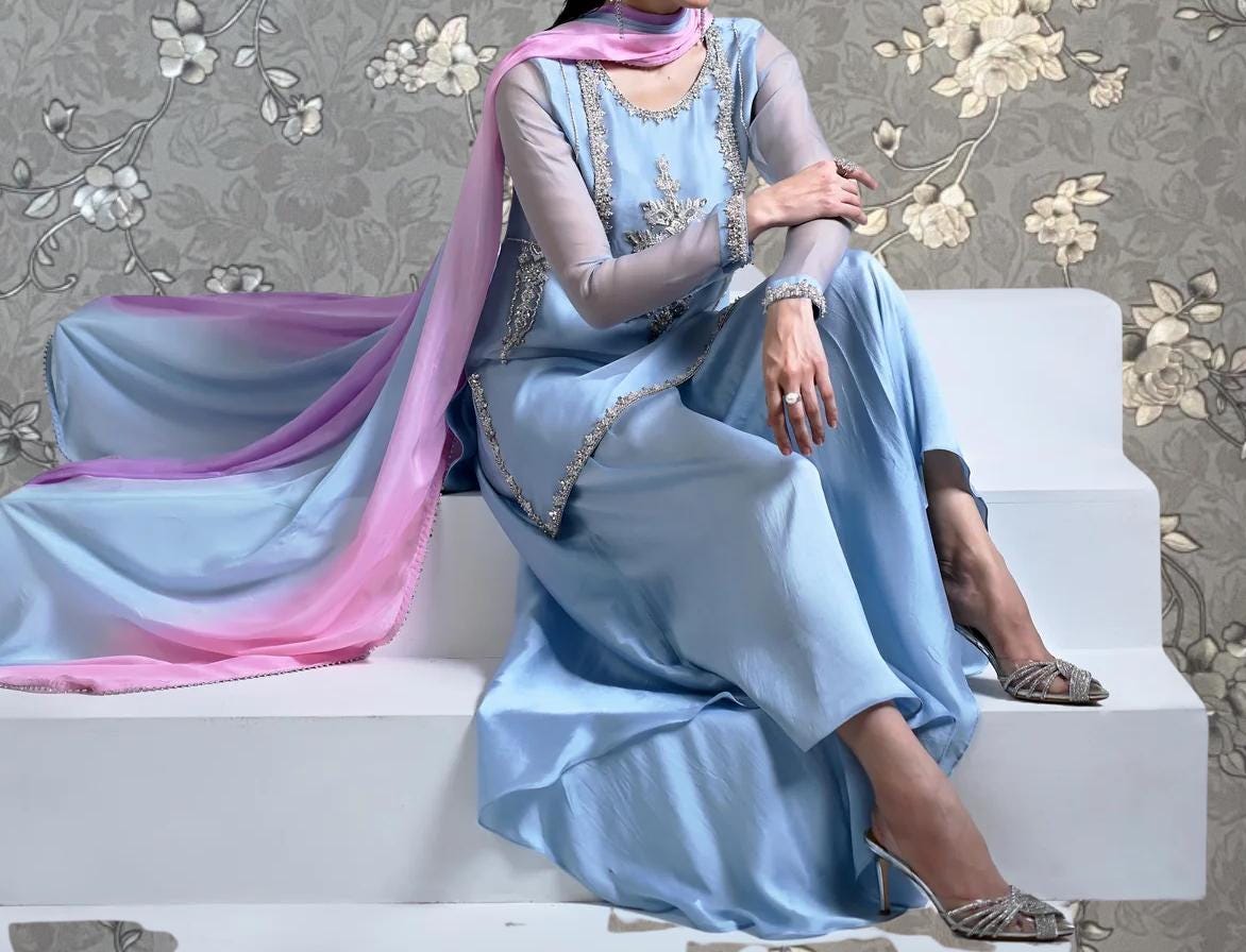 A woman wearing a blue dress with a pink and purple sash is sitting on a white step.