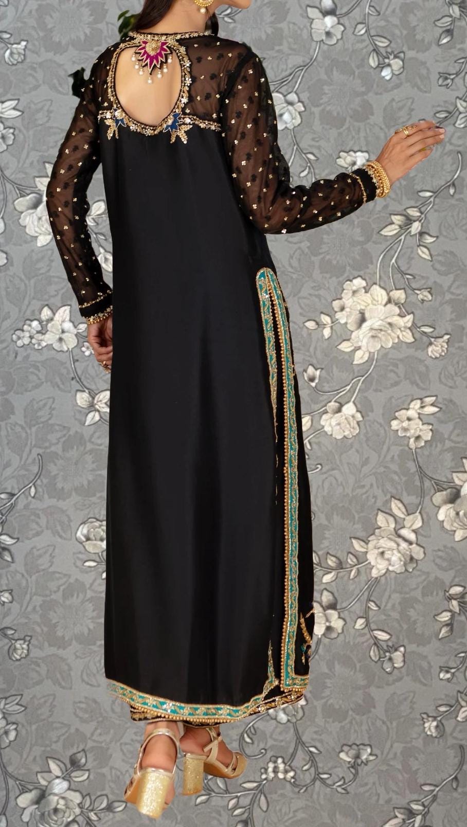 a woman wearing a black dress with a floral pattern and gold accents. She is standing against a gray floral background.