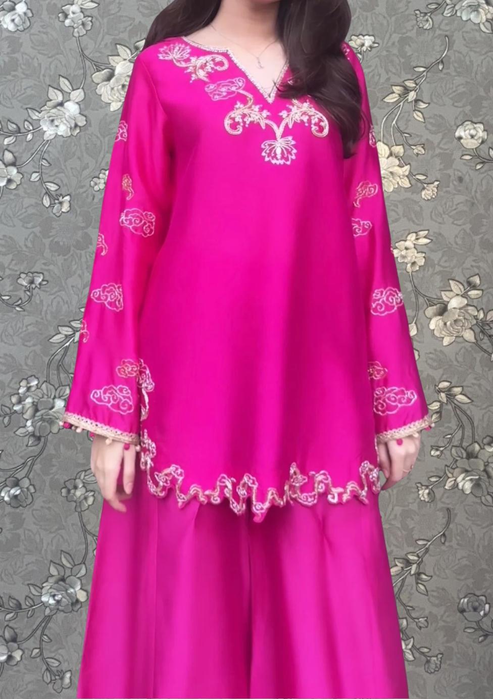 A woman wearing a bright pink dress with intricate embroidery on the front.