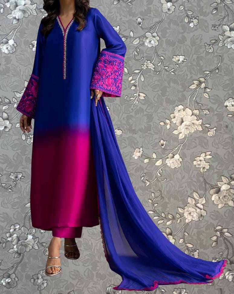 A woman wearing a long blue dress with pink accents, standing against a gray floral background.