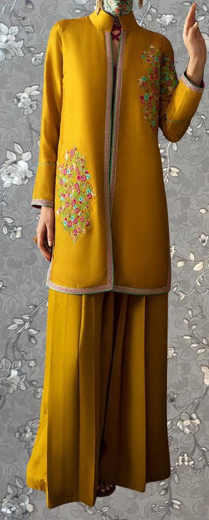 A person wearing a vibrant yellow dress with floral embroidery on the sleeves and a matching skirt, standing against a gray floral background.