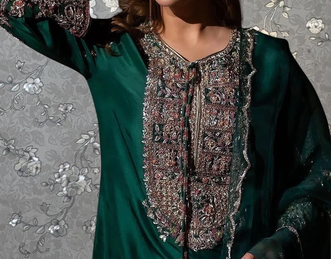 A close-up of a person wearing a green dress with intricate embroidered patterns and designs.