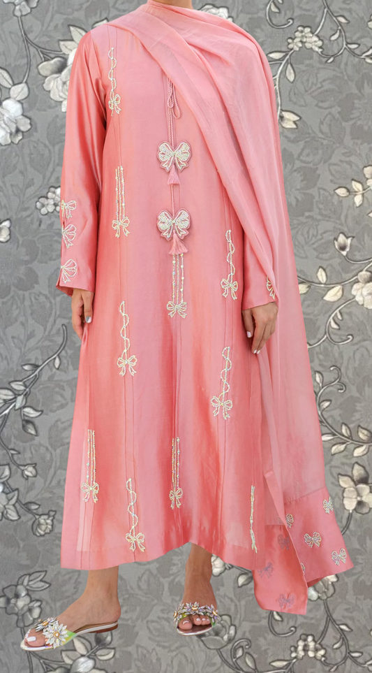 A person wearing a long pink dress with white floral embroidery and a matching pink shawl.