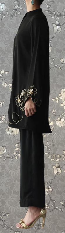 A person wearing a black outfit with gold floral embroidery stands against a gray floral background.