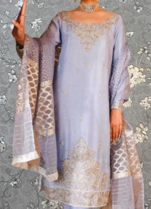 A woman wearing a lavender dress with intricate embroidery and a matching shawl stands against a gray floral background.