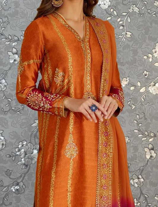 A woman wearing an orange and gold dress with intricate embroidery and a matching shawl. She is holding a blue ring in her hand.