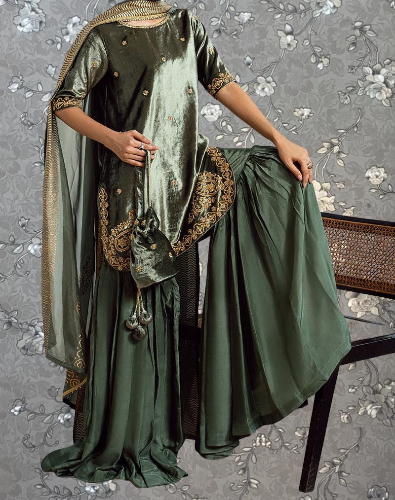 A person wearing a green and gold dress with a long skirt, standing in front of a floral patterned background.