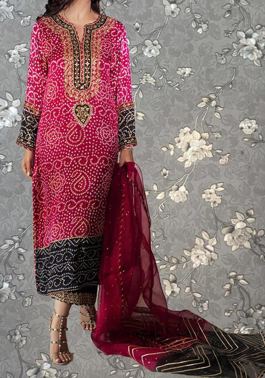 A woman wearing a long pink and black dress with gold accents, standing against a gray floral background.