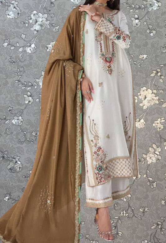 A woman wearing a white and gold dress with intricate embroidery, standing against a gray floral background.