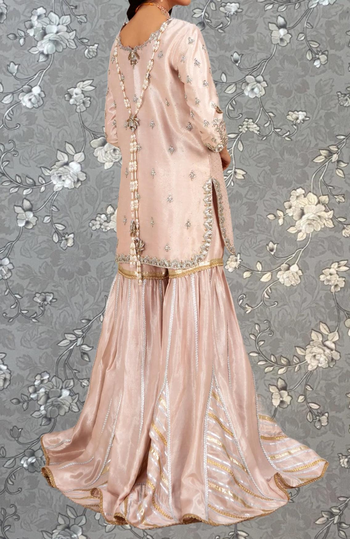 A woman wearing a long, pink dress with intricate embroidery and a high slit on the back.