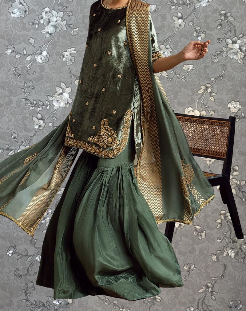 A person wearing a green and gold dress with intricate embroidery, standing in front of a floral patterned background.