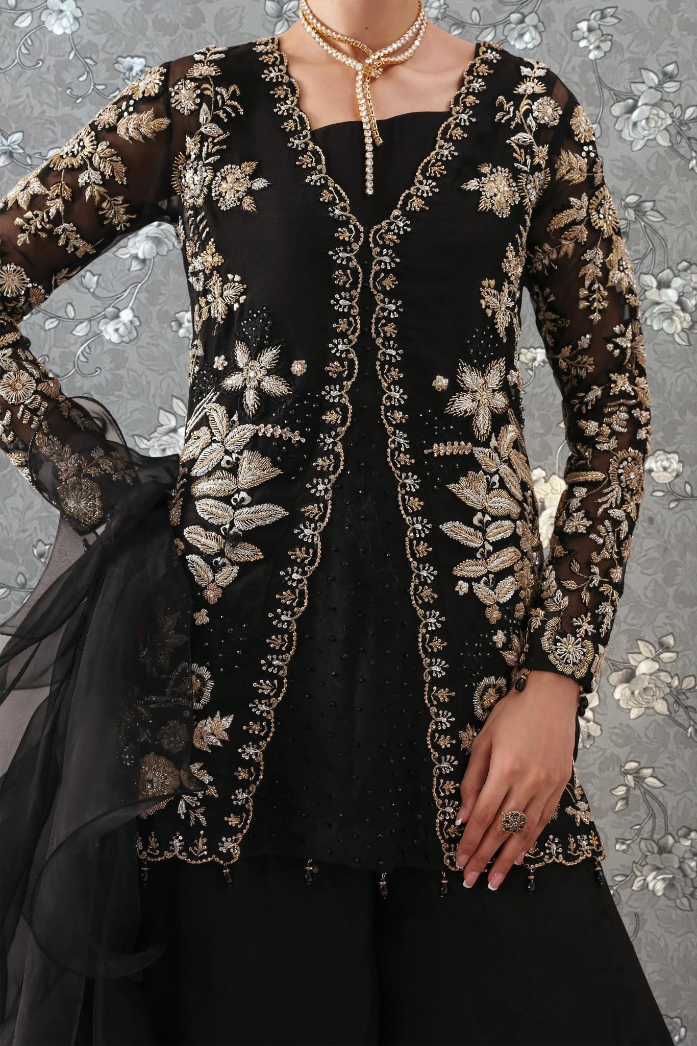 A woman wearing a black and gold dress with intricate embroidery and a black jacket with gold accents.