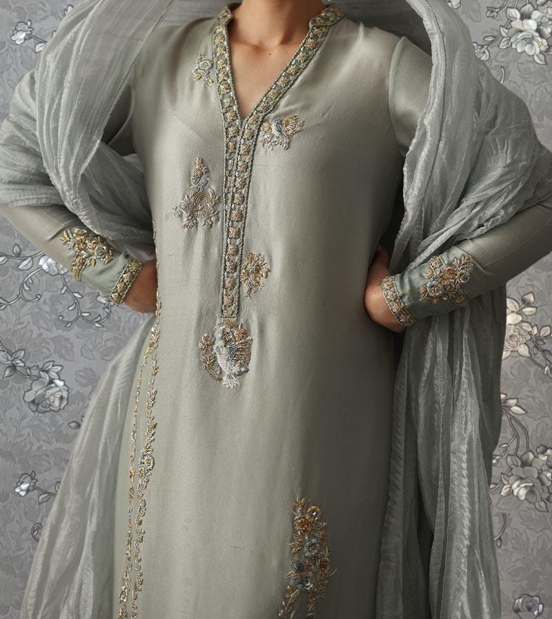 A person wearing a gray dress with intricate embroidered designs on the front.