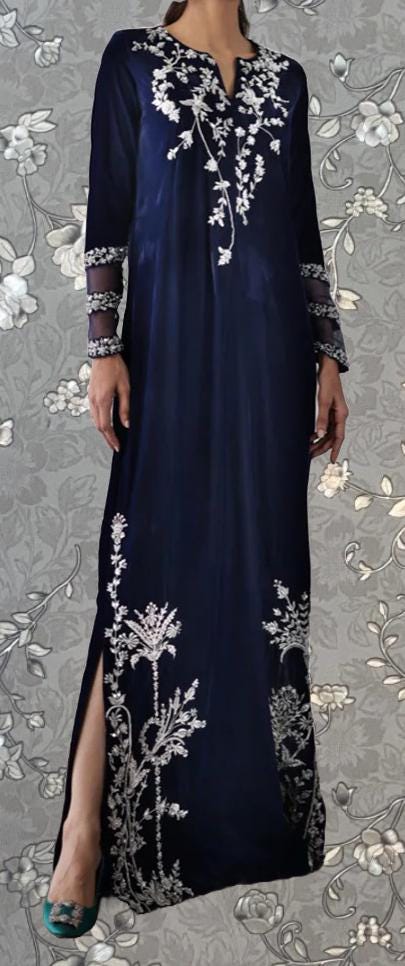 A woman wearing a long navy blue dress with white floral embroidery on the sleeves and hem.