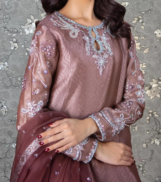 A woman wearing a pink dress with intricate embroidery and a matching shawl stands against a floral background.