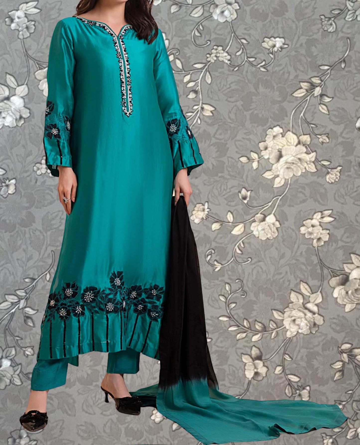 A woman wearing a long, turquoise dress with floral embroidery and holding a black shawl.