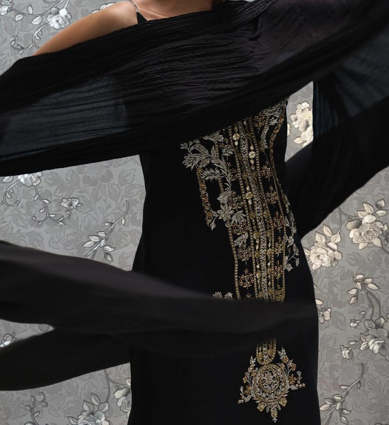 A person wearing a black dress with intricate gold embroidery stands against a floral background.