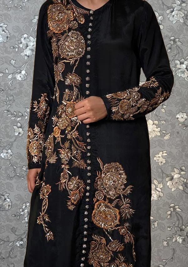 A person wearing a long black dress with gold embroidered designs on the sleeves and collar.