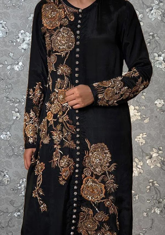 A person wearing a long black dress with gold embroidered designs on the sleeves and collar.