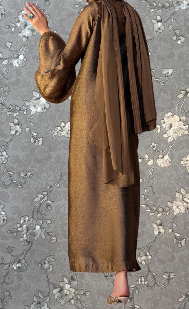 a person wearing a long, brown dress with a scarf draped over the back, standing against a gray floral background.