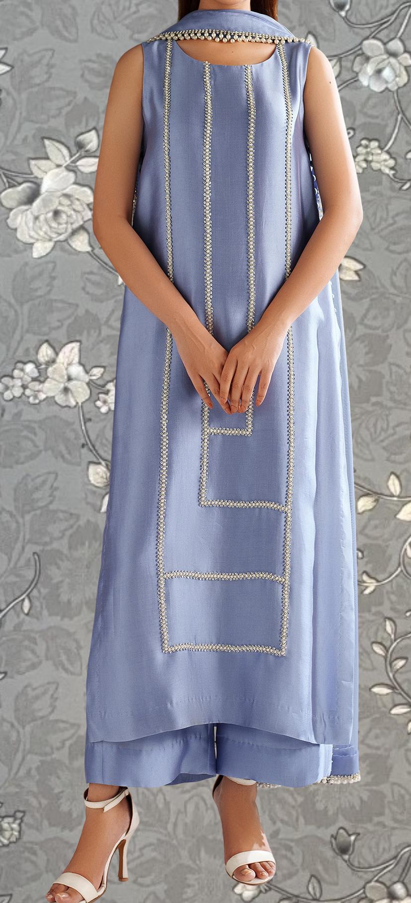 A person wearing a sleeveless blue dress with a geometric pattern and white accents, standing against a gray floral background.