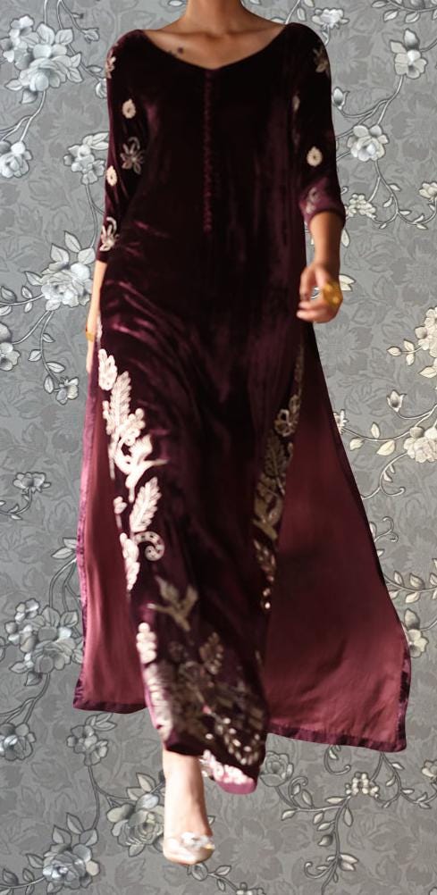 A woman wearing a long, burgundy velvet dress with intricate embroidered designs on the bodice and skirt.