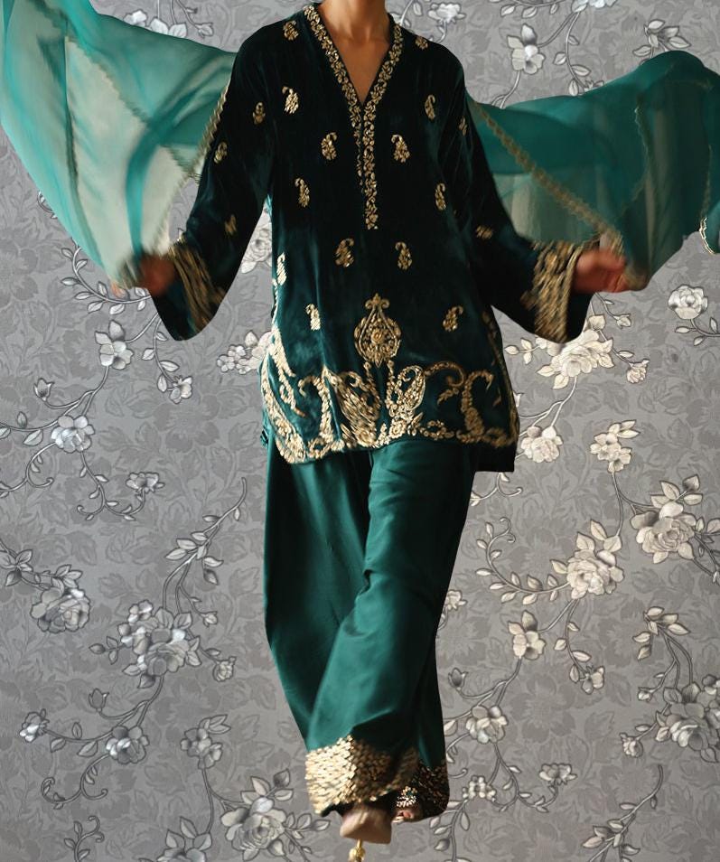 A person wearing a green and gold embroidered outfit with a matching green scarf is shown against a gray floral background.