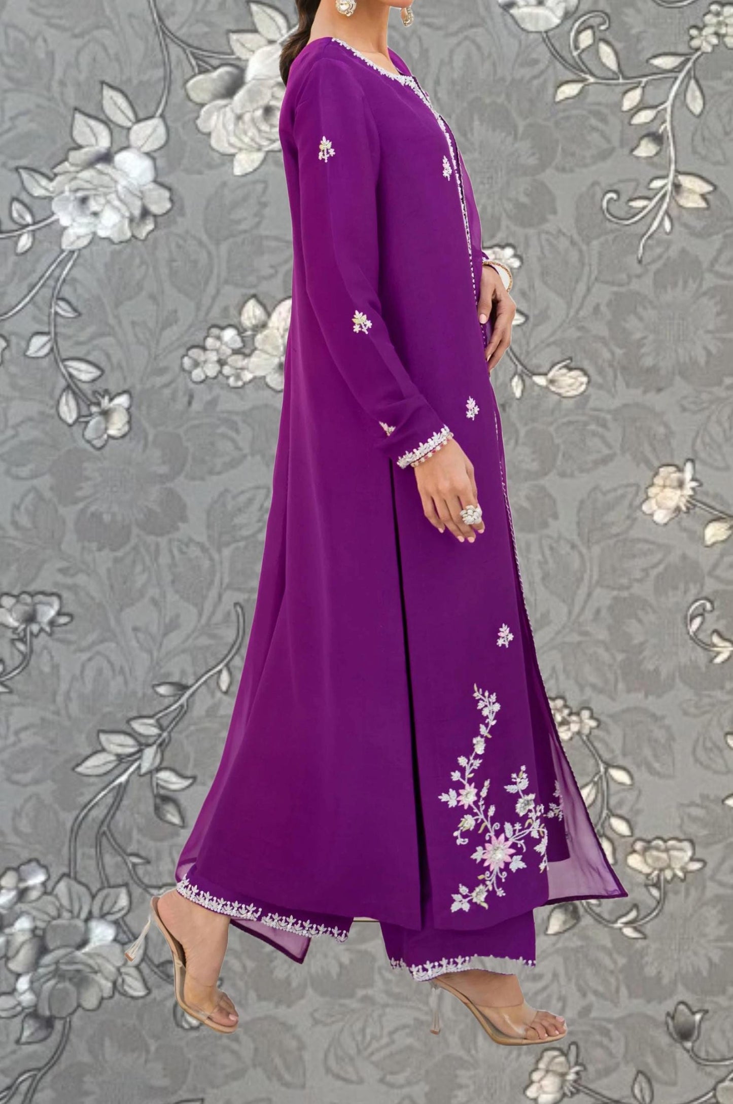A woman wearing a long purple dress with white floral embroidery stands against a gray floral background.