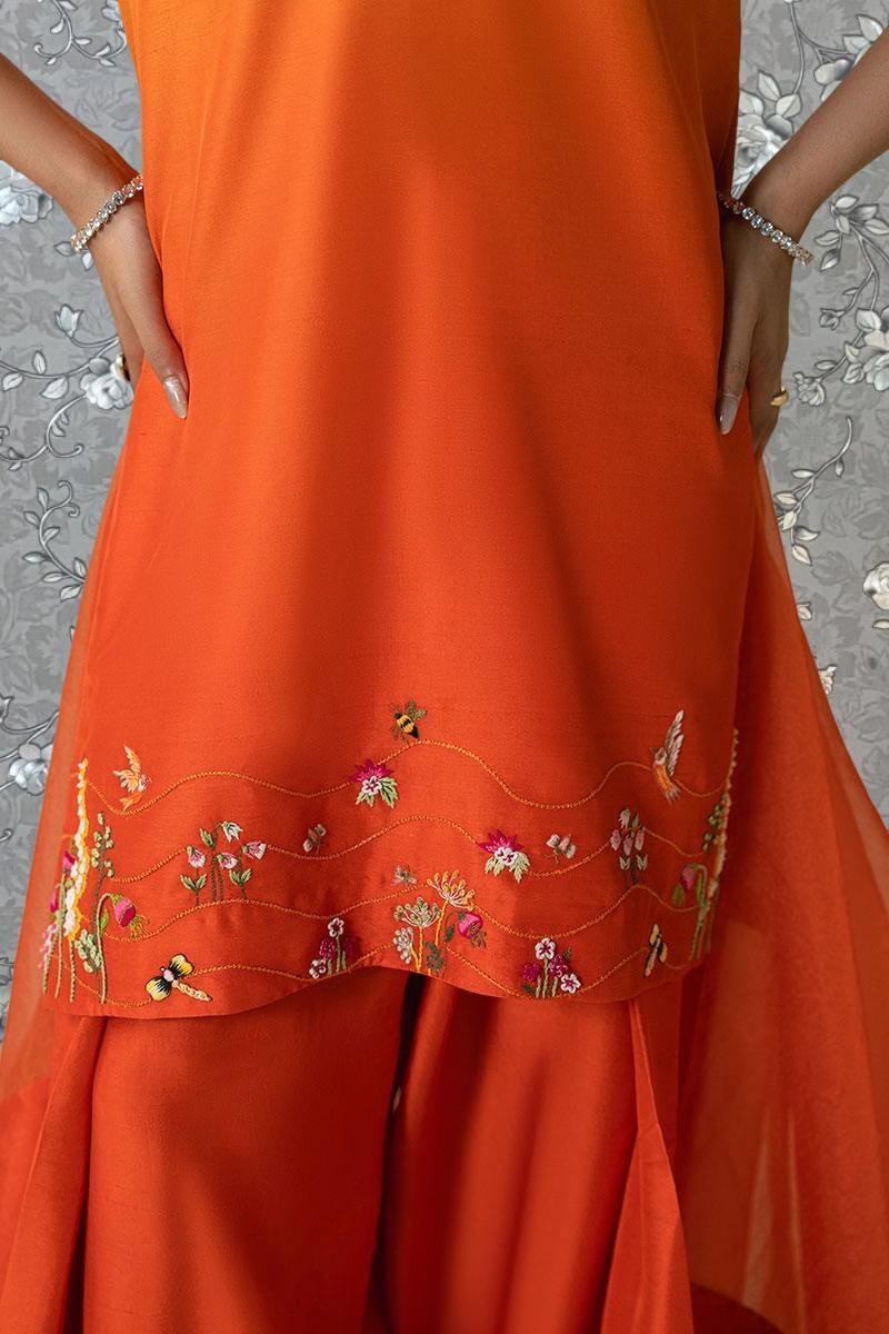 A close-up view of a person wearing an orange dress with intricate embroidered designs, including flowers and butterflies.