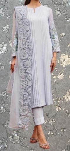 A woman wearing a long, light-colored dress with intricate lace detailing and floral embroidery.
