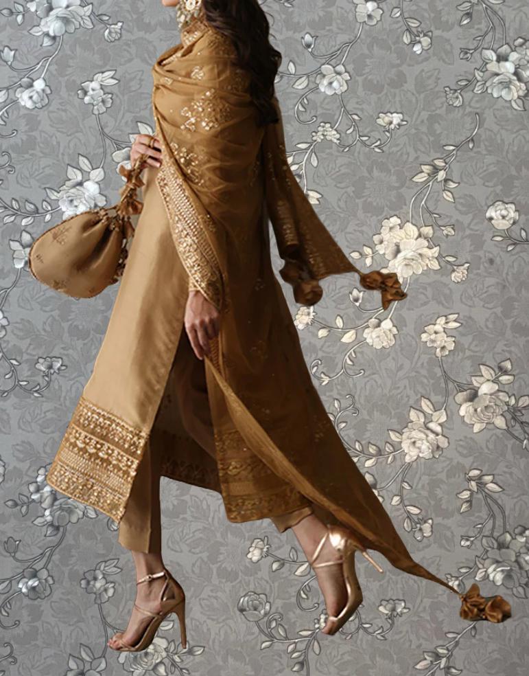 A woman wearing a long, gold-colored dress with intricate embroidery, holding a small purse, and wearing high heels, standing against a gray floral background.