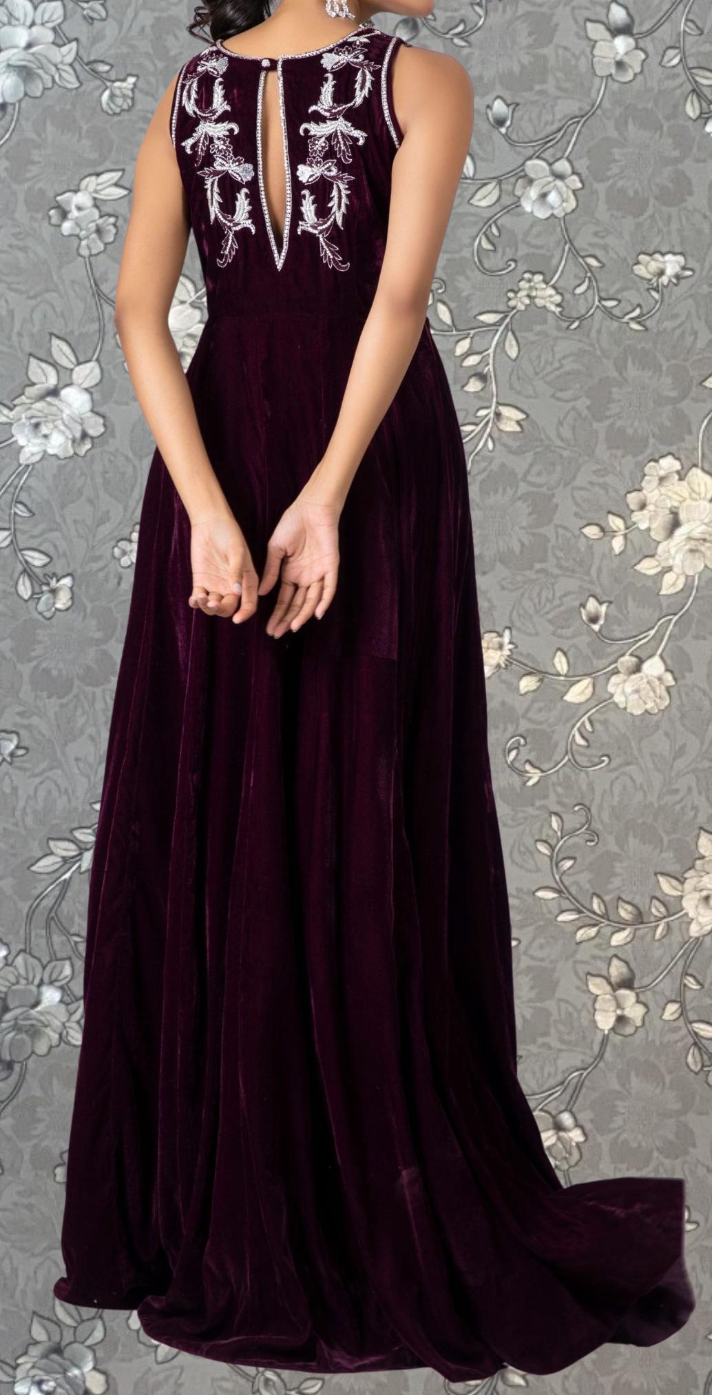 A woman wearing a long, burgundy velvet dress with white embroidered designs on the back.