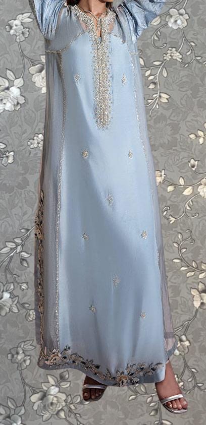 A woman wearing a long, light blue dress with intricate embroidery and floral patterns.