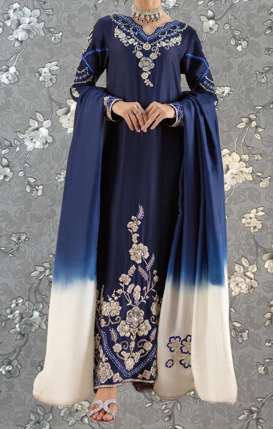 A woman wearing a blue and white dress with intricate embroidery and floral patterns, standing against a gray floral background.