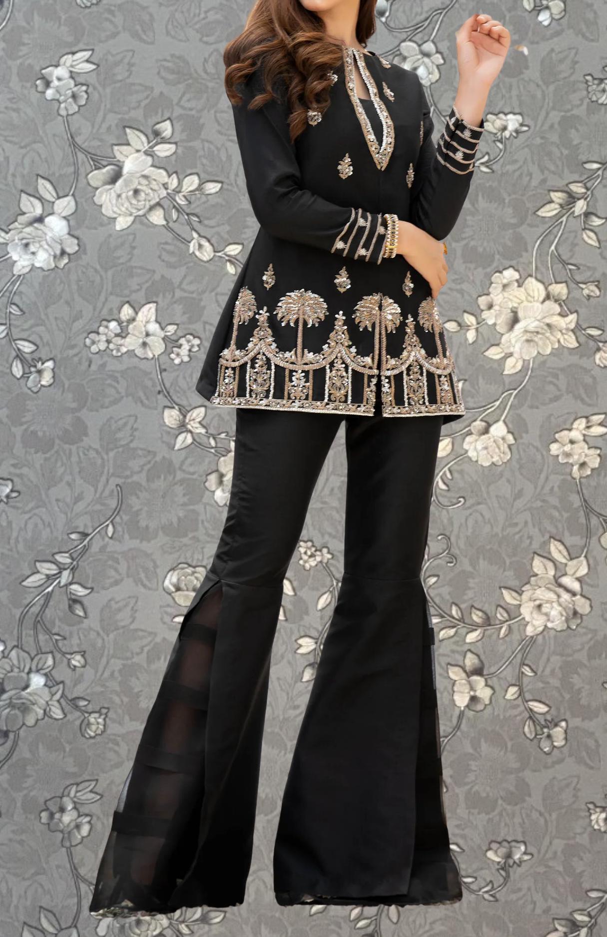 A woman wearing a black and gold dress with a floral pattern, standing against a gray floral background.