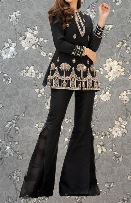 A woman wearing a black and gold dress with a floral pattern, standing against a gray floral background.