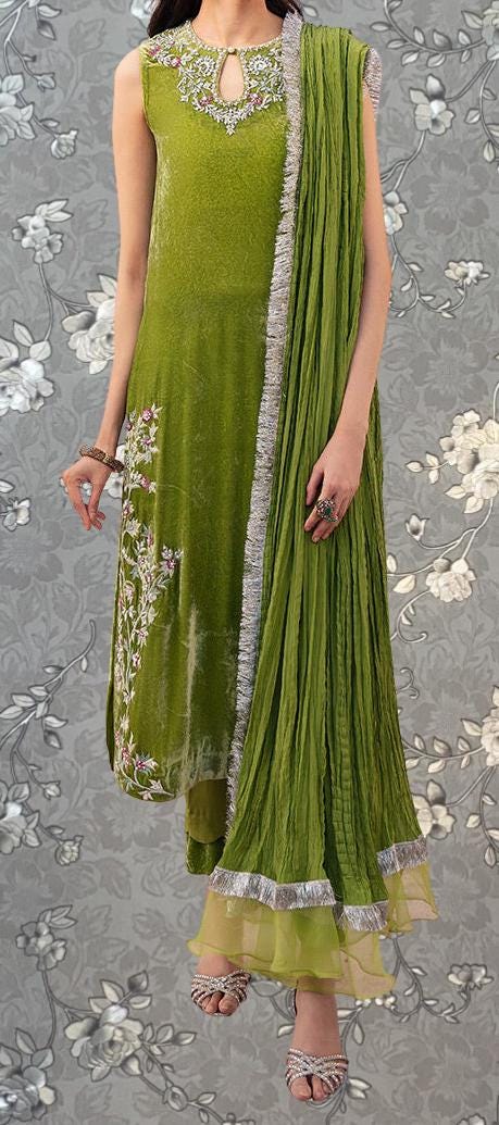 A woman wearing a green dress with a matching green shawl, standing against a gray floral background.