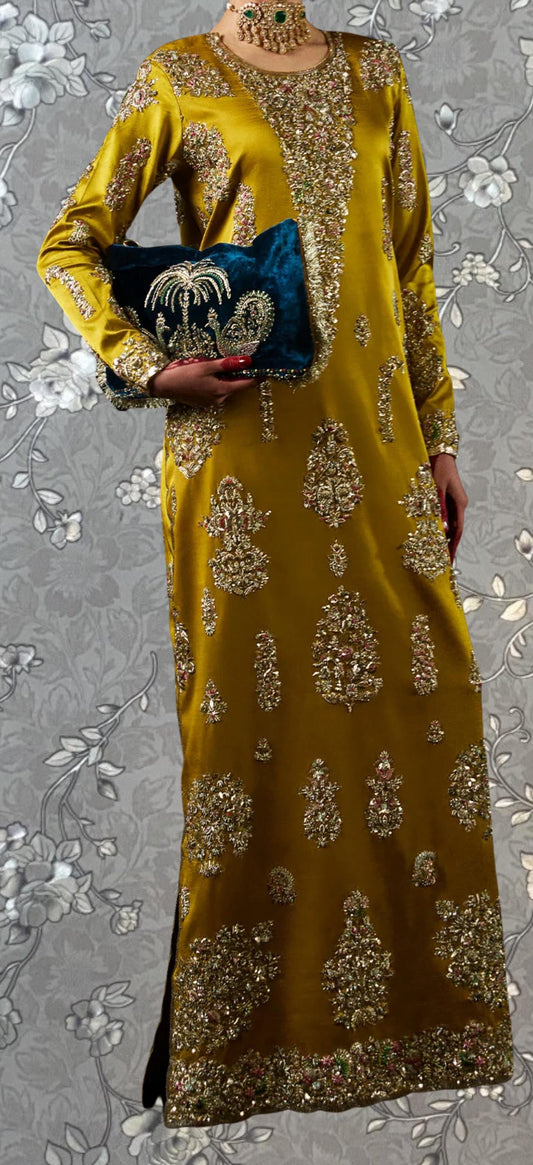 A woman wearing a long, gold and yellow dress with intricate embroidery and a matching gold necklace. She is holding a blue clutch purse.