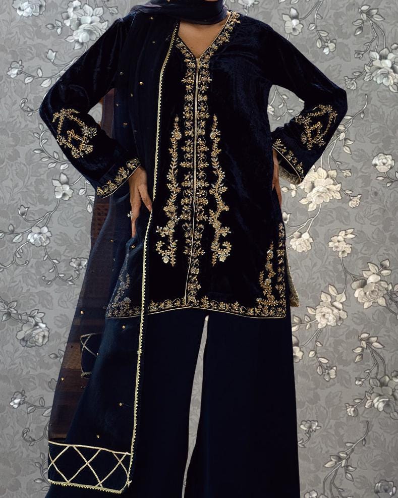 A person wearing a black velvet dress with gold embroidery and a matching black shawl.
