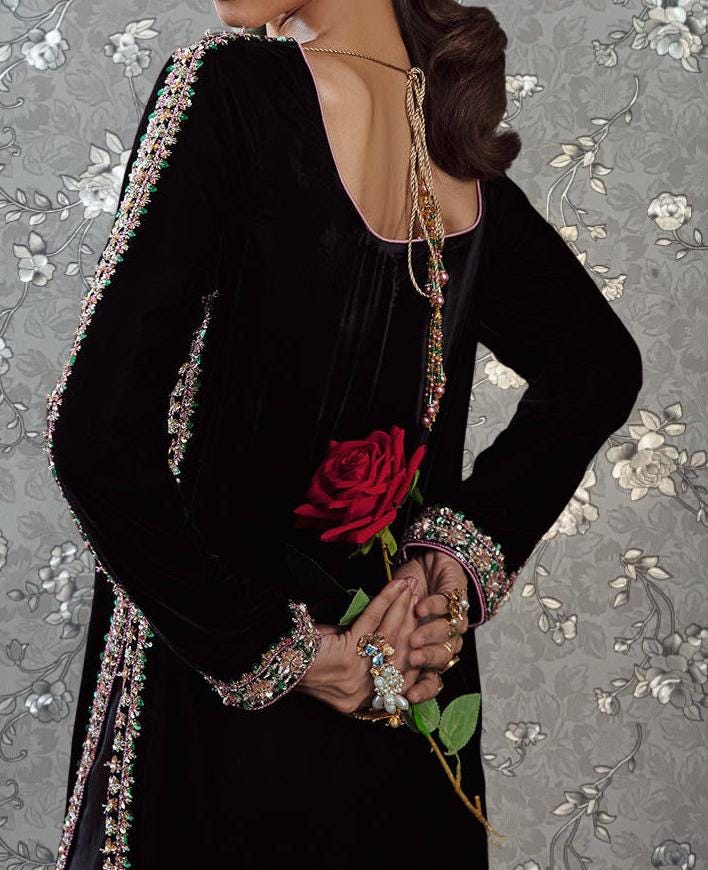A woman wearing a black dress with a red rose and jewelry poses with her back to the camera.