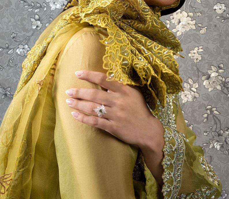 A close-up of a person's hand wearing a ring, with a yellow and green patterned dress and a scarf draped over their shoulder.
