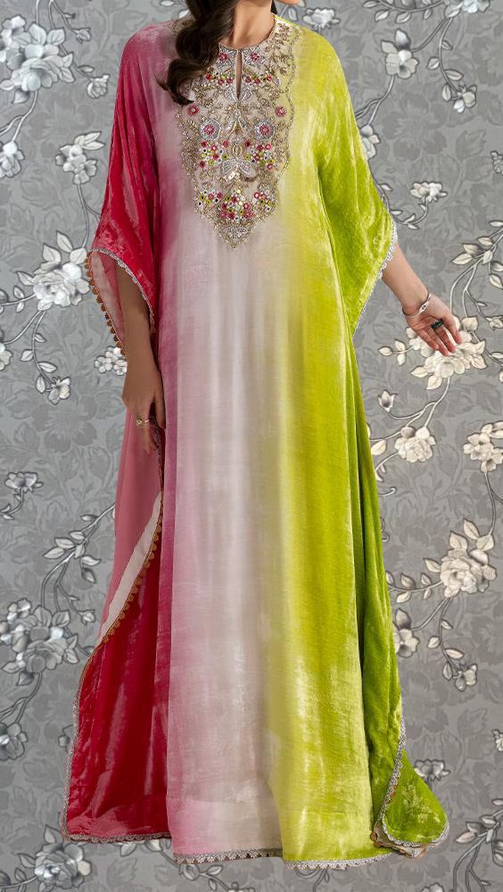 A woman wearing a long, colorful dress with a floral pattern. The dress has a mix of pink, green, and white colors, and the woman is standing against a gray floral background.