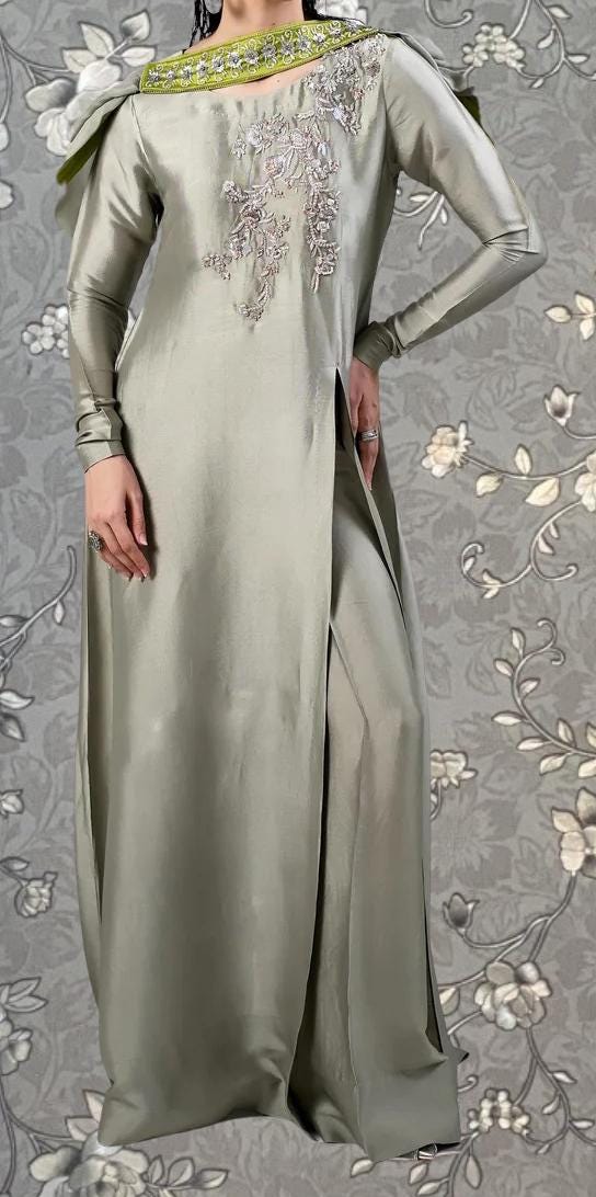 A person wearing a long, gray dress with intricate embroidery and a green accent on the neckline.