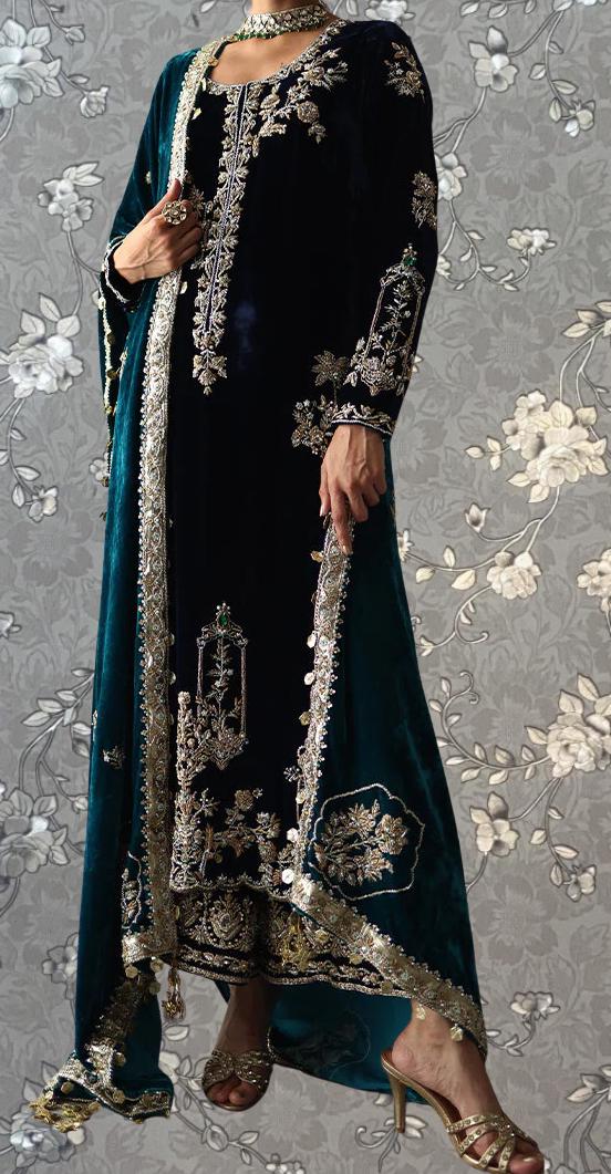 A woman wearing an ornate, long black dress with intricate gold embroidery and a matching green velvet shawl. She is holding a small clutch in her hand.