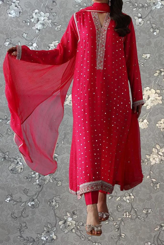 A woman wearing a long red dress with white polka dots and a matching red shawl, standing against a gray floral background.