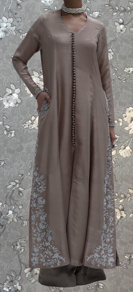 A woman wearing a long, beige dress with intricate embroidered patterns on the sides.