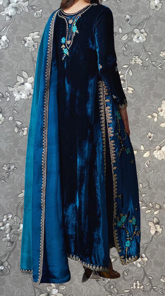 A woman wearing a long, blue velvet dress with intricate embroidery on the back and a matching blue shawl draped over her shoulders.