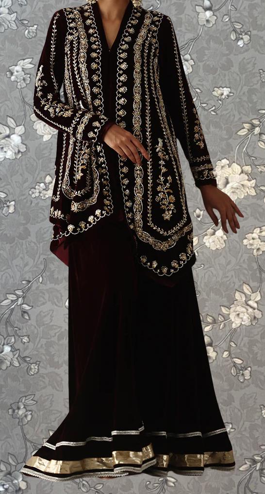 A person wearing a long, black dress with intricate gold embroidery and a matching jacket.