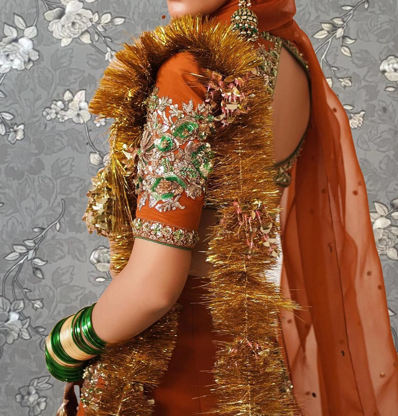 A woman wearing an ornate, gold and red dress with a long, decorative shawl and gold tassels. She is also wearing green and gold jewelry.
